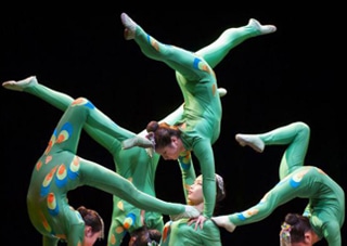 Cirque Diabolo Acrobats Form a human tower wearing green suits on a black background.